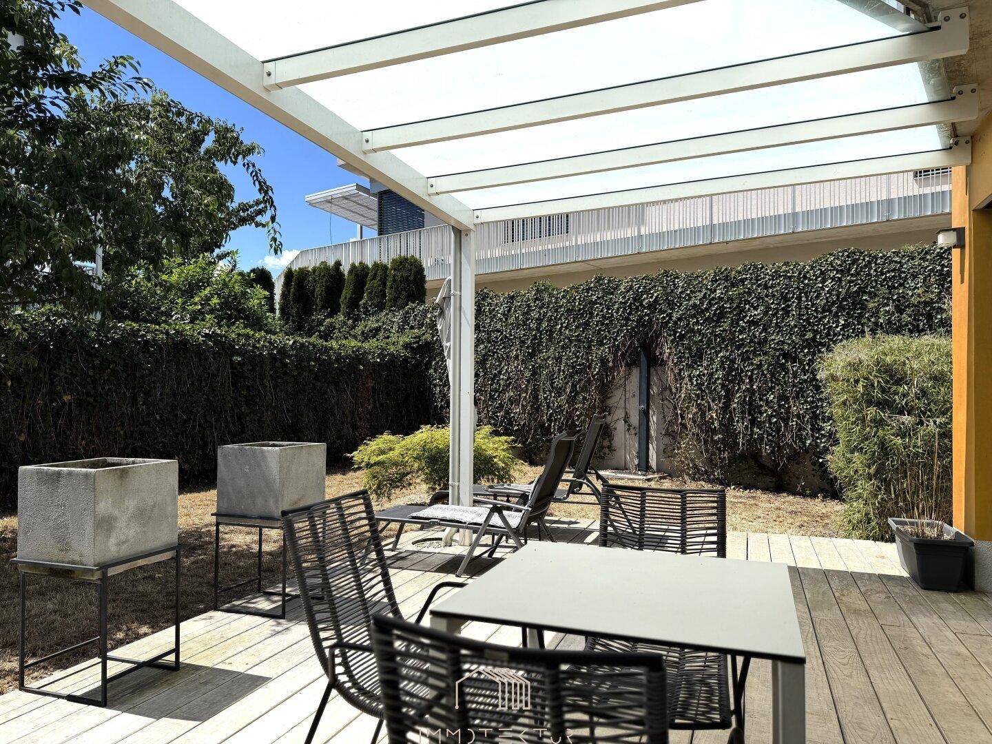Überdachte Terrasse mit modernen Gartenmöbeln und Blick auf die grüne Hecke.