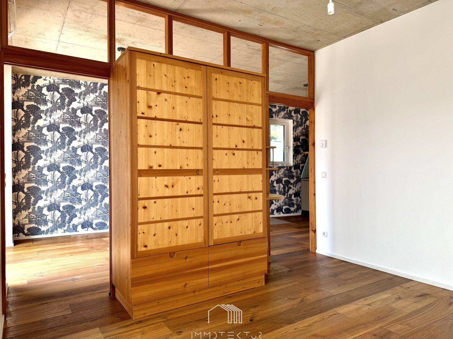 Geräumiger Flur mit großem Holzschrank, Holzboden und Zugang zu Zimmern mit gemusterter Tapete.