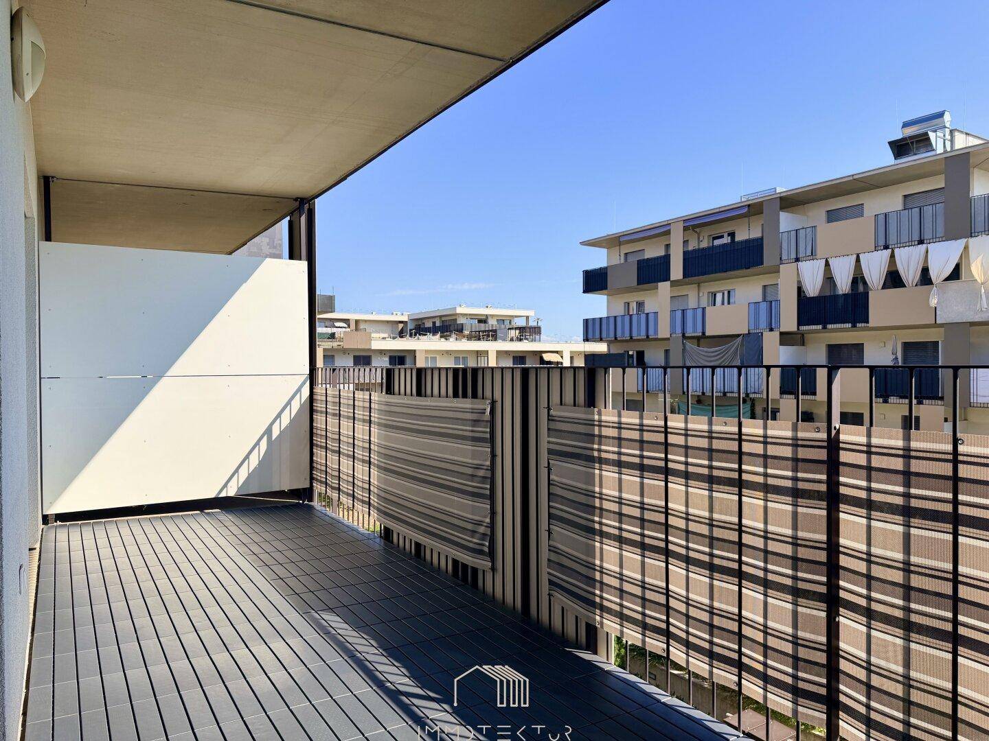 Geräumiger Balkon mit Holzboden und Blick auf die umliegenden Gebäude.