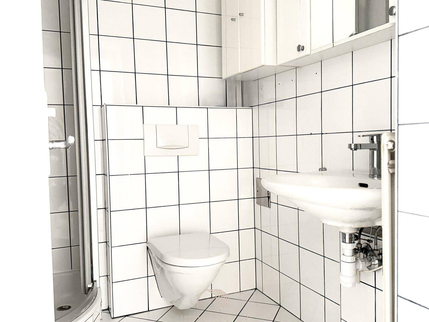 Modernes Badezimmer mit weißen Fliesen, Dusche und wandhängendem WC.
