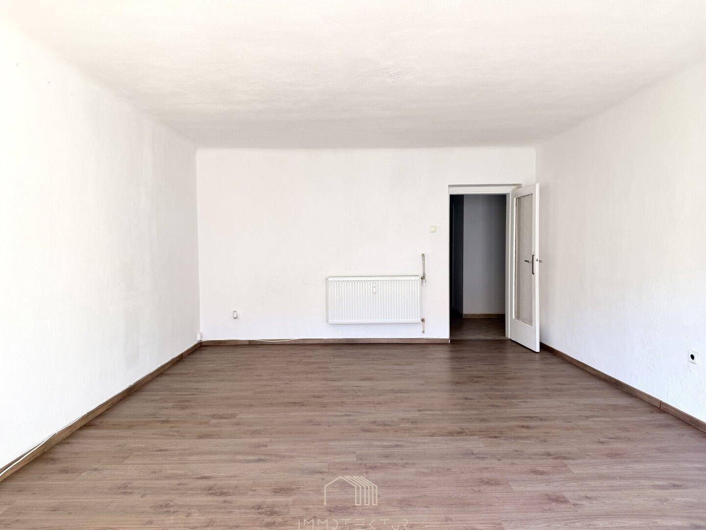 Geräumiges, leeres Zimmer mit Laminatboden und weiß gestrichenen Wänden.