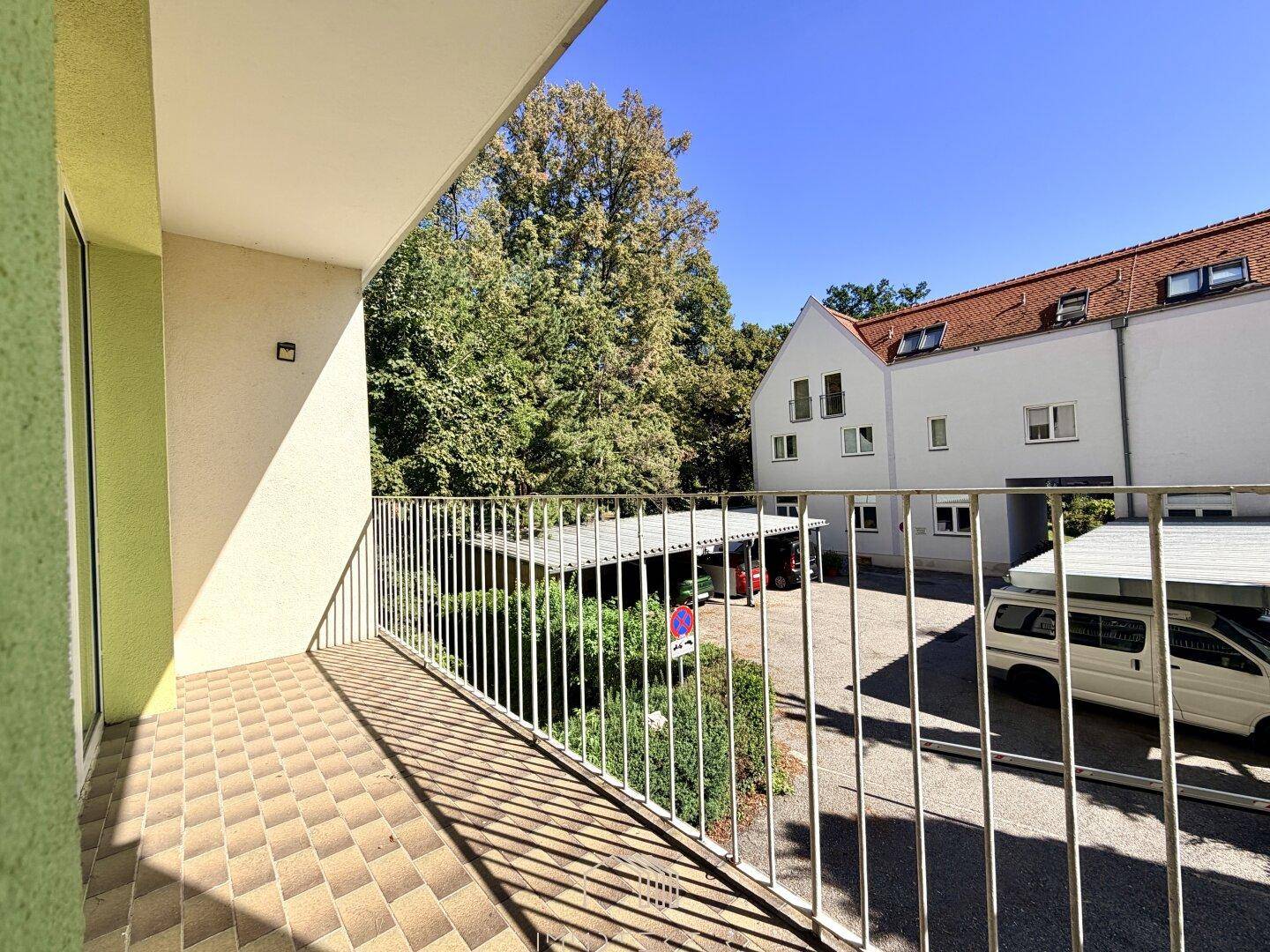 Geräumiger Balkon mit Fliesenboden und Blick auf den Innenhof und Parkplätze.