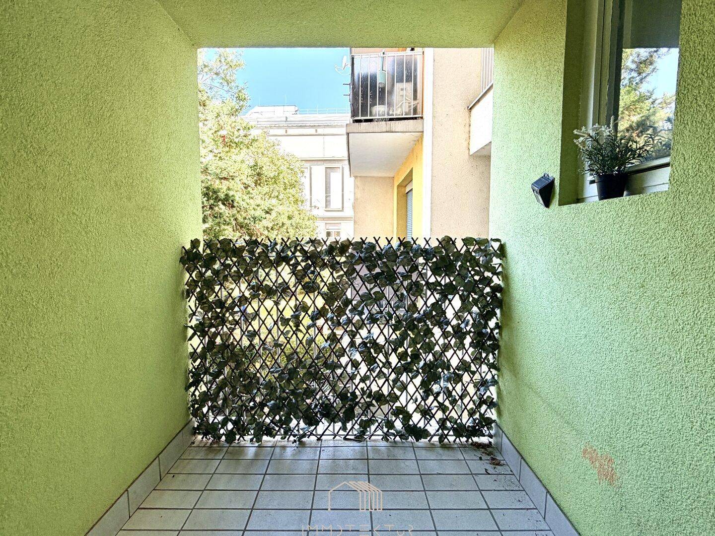 Kleiner Balkon mit grünem Sichtschutz und Blick auf die Nachbargebäude.