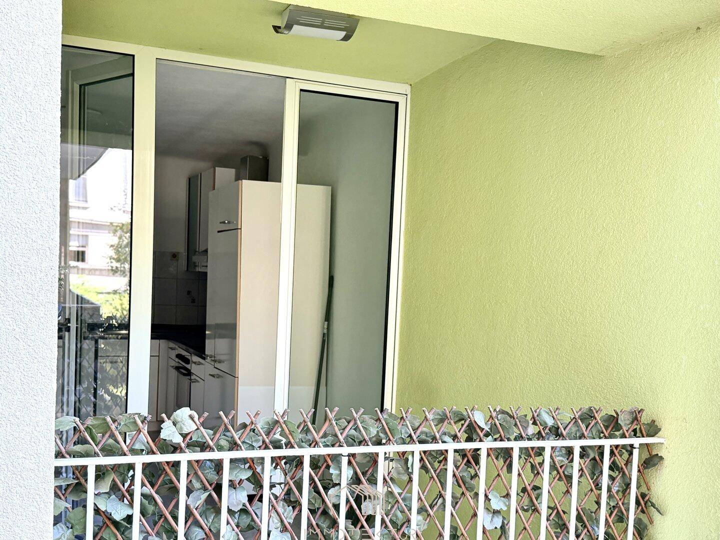 Balkon mit grünem Sichtschutz und Einblick in die angrenzende Küche.