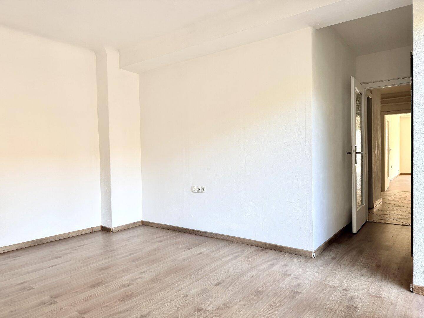 Leeres Zimmer mit Laminatboden und weißen Wänden, bereit zur individuellen Gestaltung.