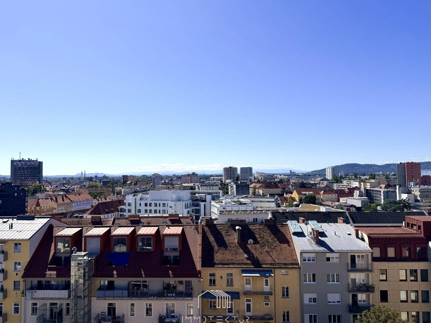 Weitläufiger Blick über die Dächer der Stadt unter einem klaren blauen Himmel.