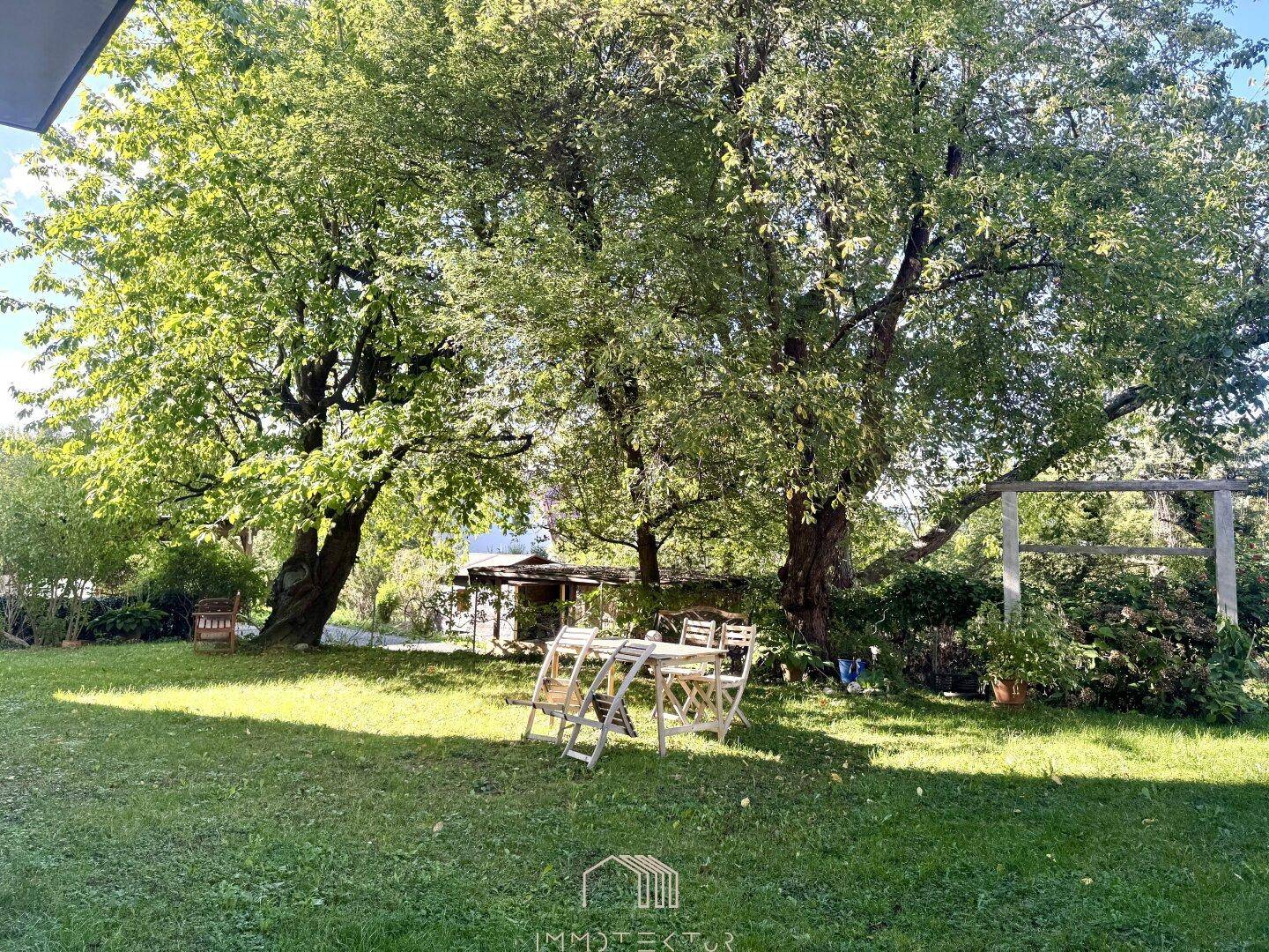 Großer Garten mit altem Baumbestand und gemütlichem Sitzbereich im Freien.
