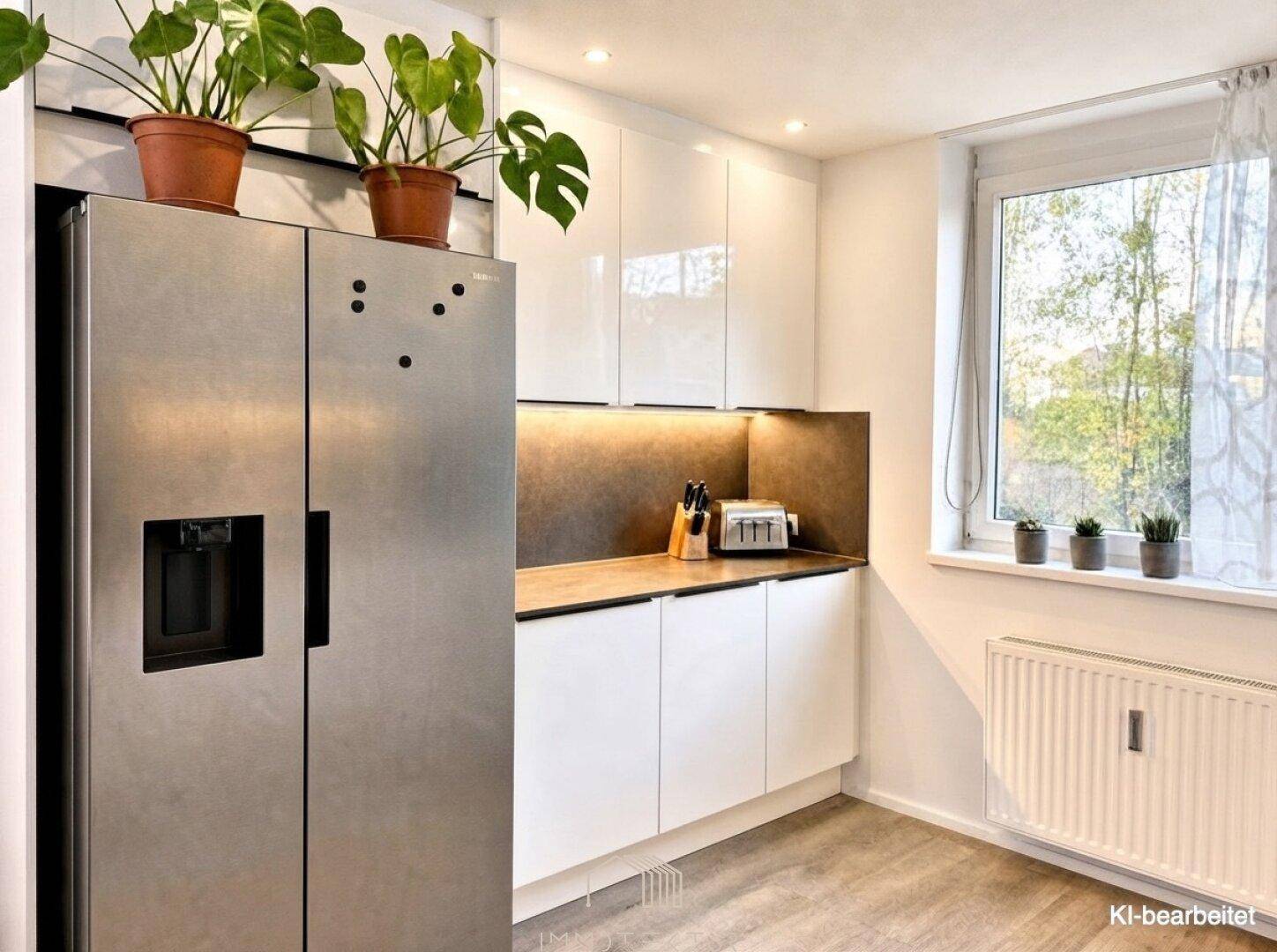 Moderne Küche mit weißen Hochglanzschränken, großem Kühlschrank und Fenster für Tageslicht.