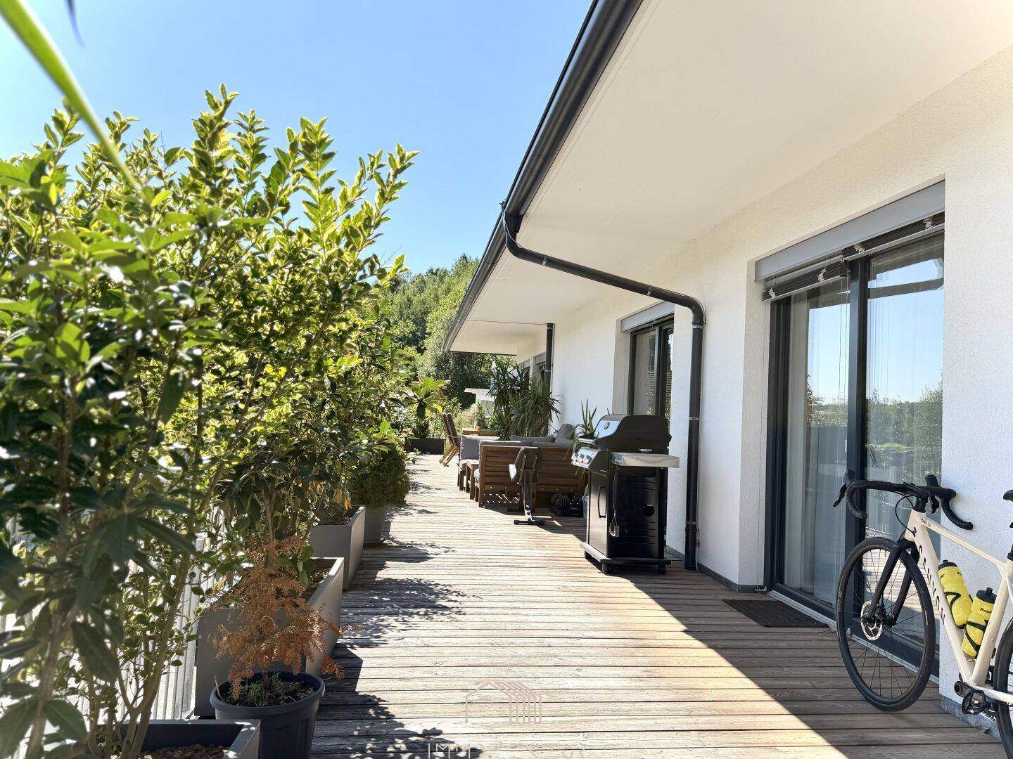 Geräumige Holzterrasse mit Grillbereich, vielen Pflanzen und Zugang zu den Innenräumen.