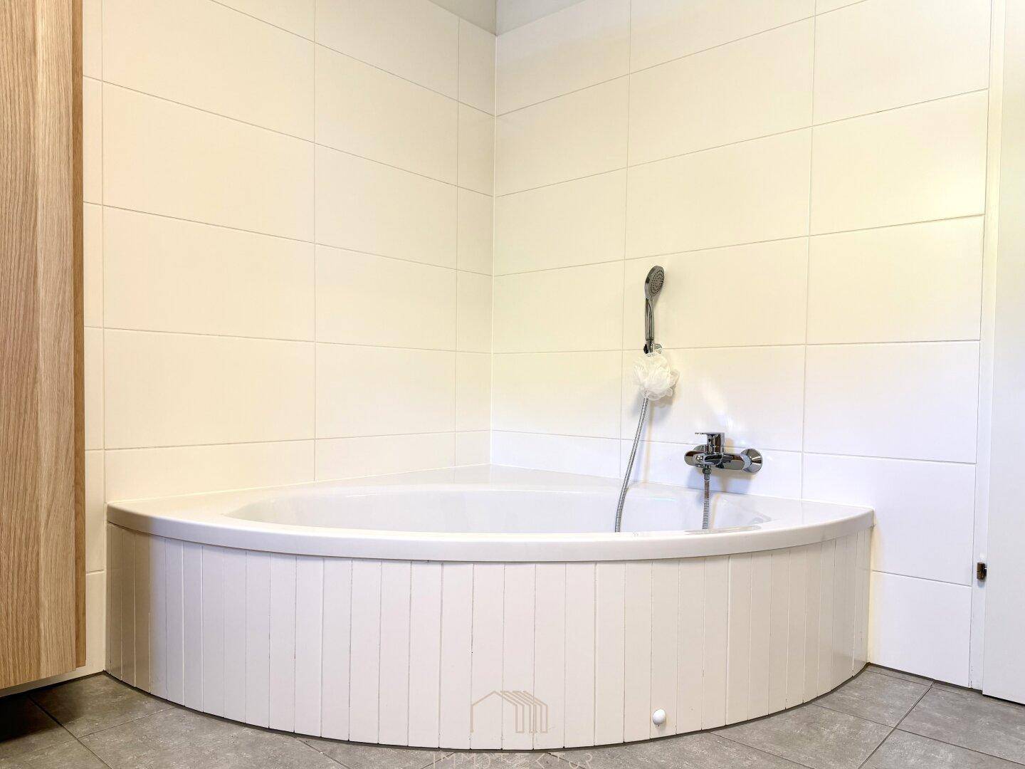 Helles Badezimmer mit einer praktischen Eckbadewanne und weißen Wandfliesen.