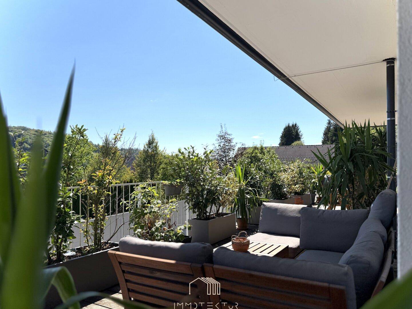 Sonnige Terrasse mit bequemen Lounge-Möbeln, vielen Pflanzen und weitem Blick ins Grüne.