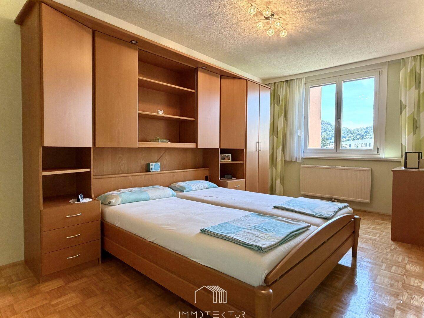Schlafzimmer mit integriertem Holzschrank, zwei Einzelbetten und Blick ins Grüne.