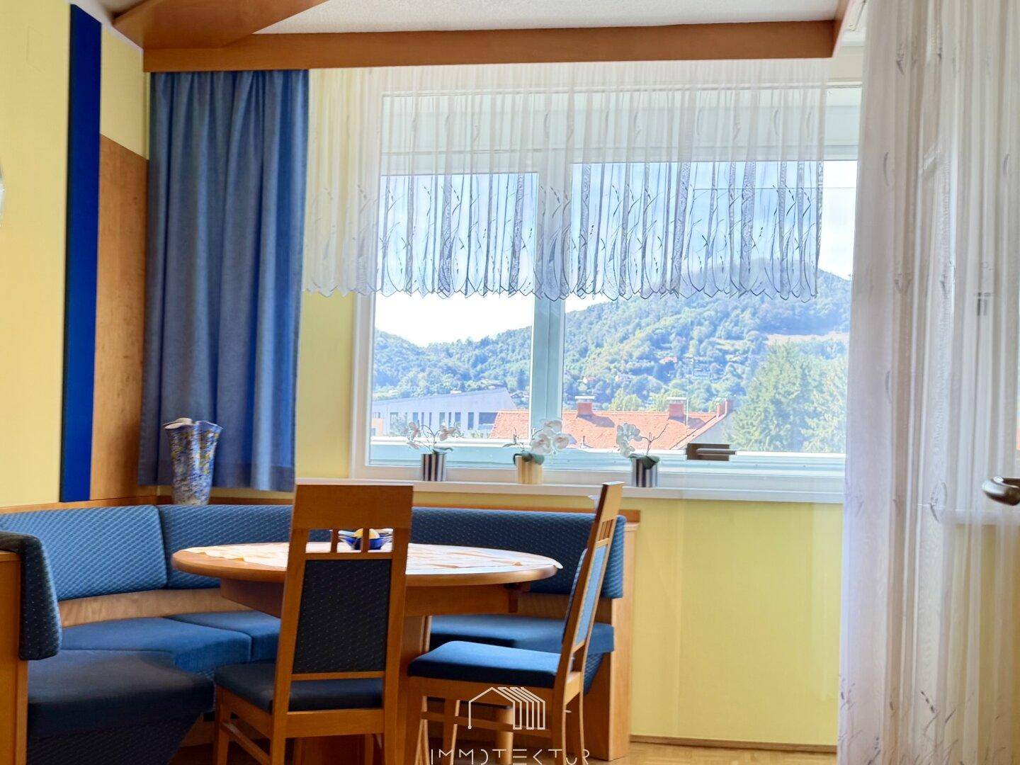 Gemütlicher Essbereich mit Eckbank, Holztisch und Bergblick durch große Fenster.