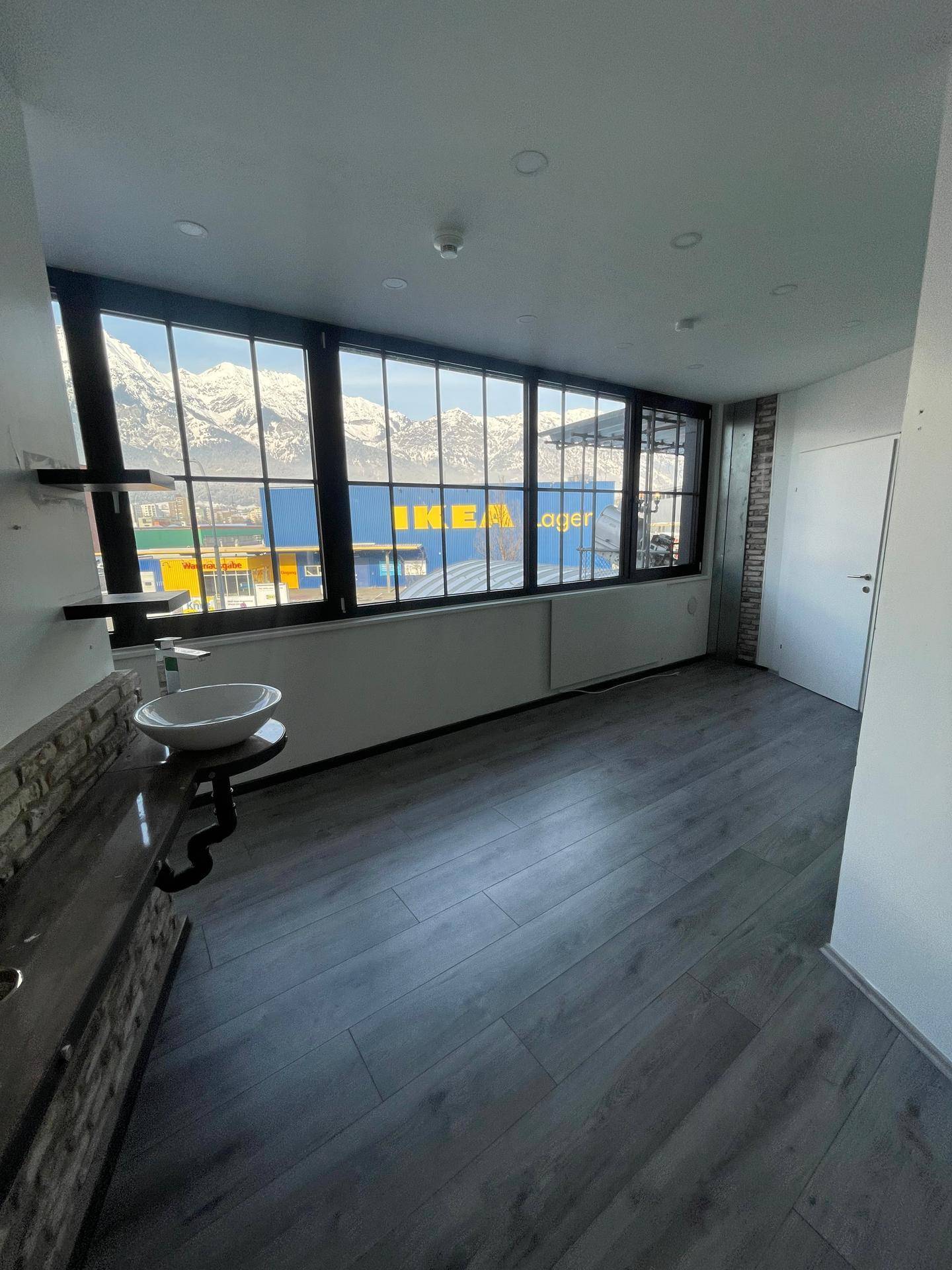 Heller Raum mit Blick auf Berge und ein IKEA-Lager, ausgestattet mit Laminatboden und einem Wandwaschbecken.