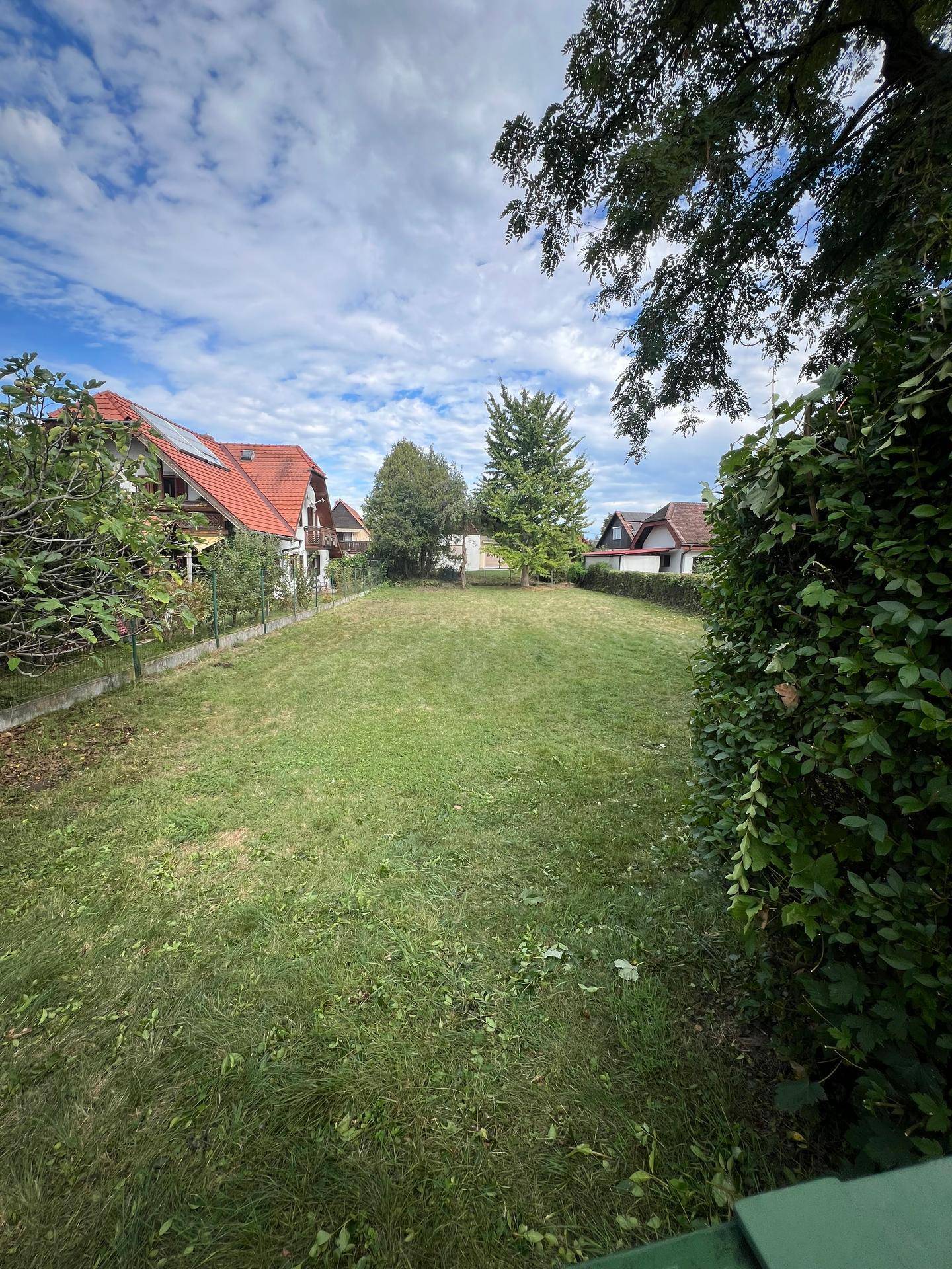 Gepflegter Garten mit Rasenfläche und Bäumen, umgeben von Wohnhäusern unter blauem Himmel.