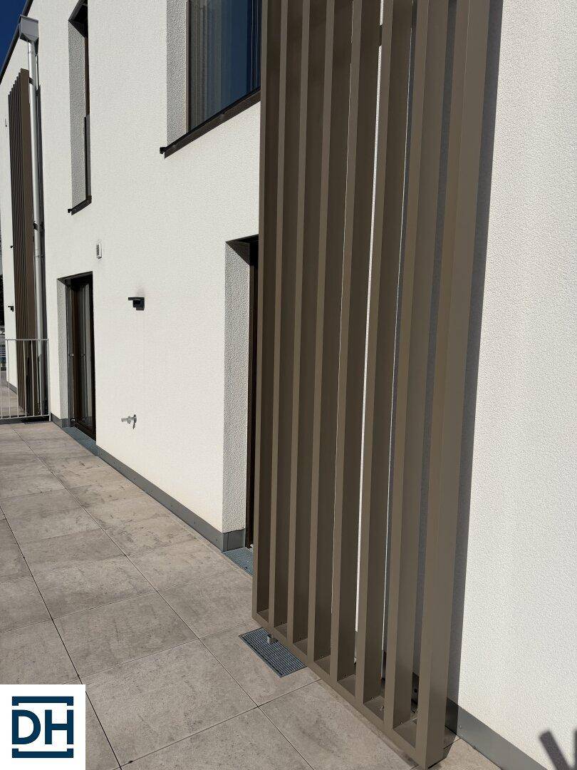 Nahaufnahme der modernen Gebäudefassade mit vertikalen Lamellen und einem Teil der gefliesten Terrasse.