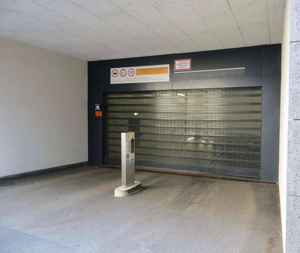 Einfahrt zu einer Tiefgarage mit Rolltor und Zugangssäule in einem modernen Gebäude.