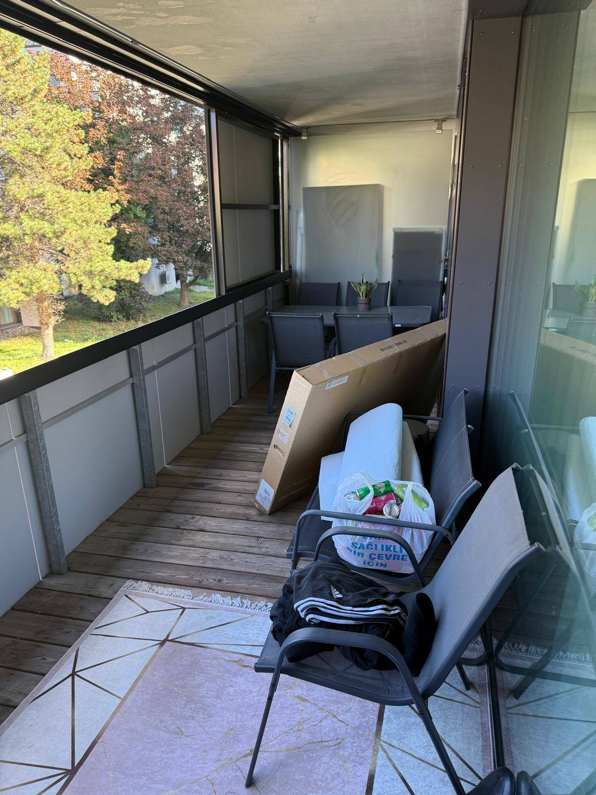 Geräumiger Balkon mit Holzrostboden, Sitzgelegenheiten und Blick auf Bäume und die Umgebung.