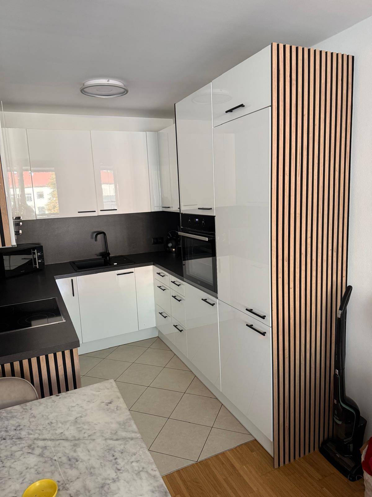 Moderne Küche mit weißen Hochglanzfronten, dunkler Arbeitsplatte und integriertem Backofen.