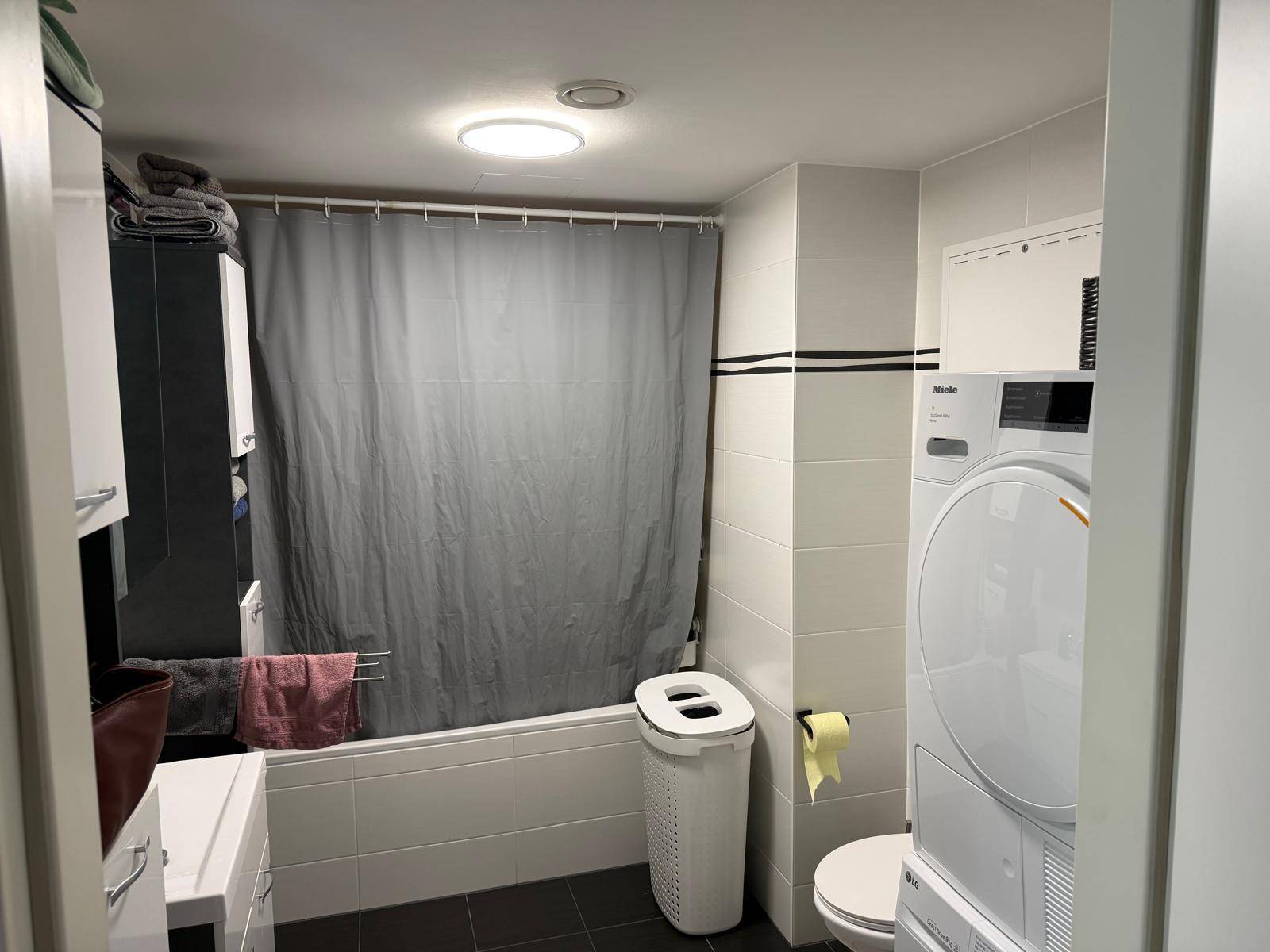 Helles Badezimmer mit Badewanne, Toilette und praktischer Waschmaschine sowie Trockner.