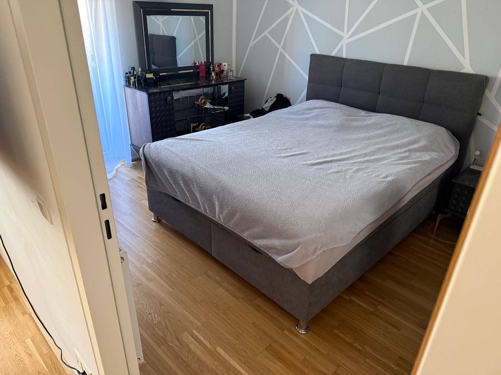 Gemütliches Schlafzimmer mit großem Doppelbett, Holzfußboden und einem Fenster mit Vorhängen.