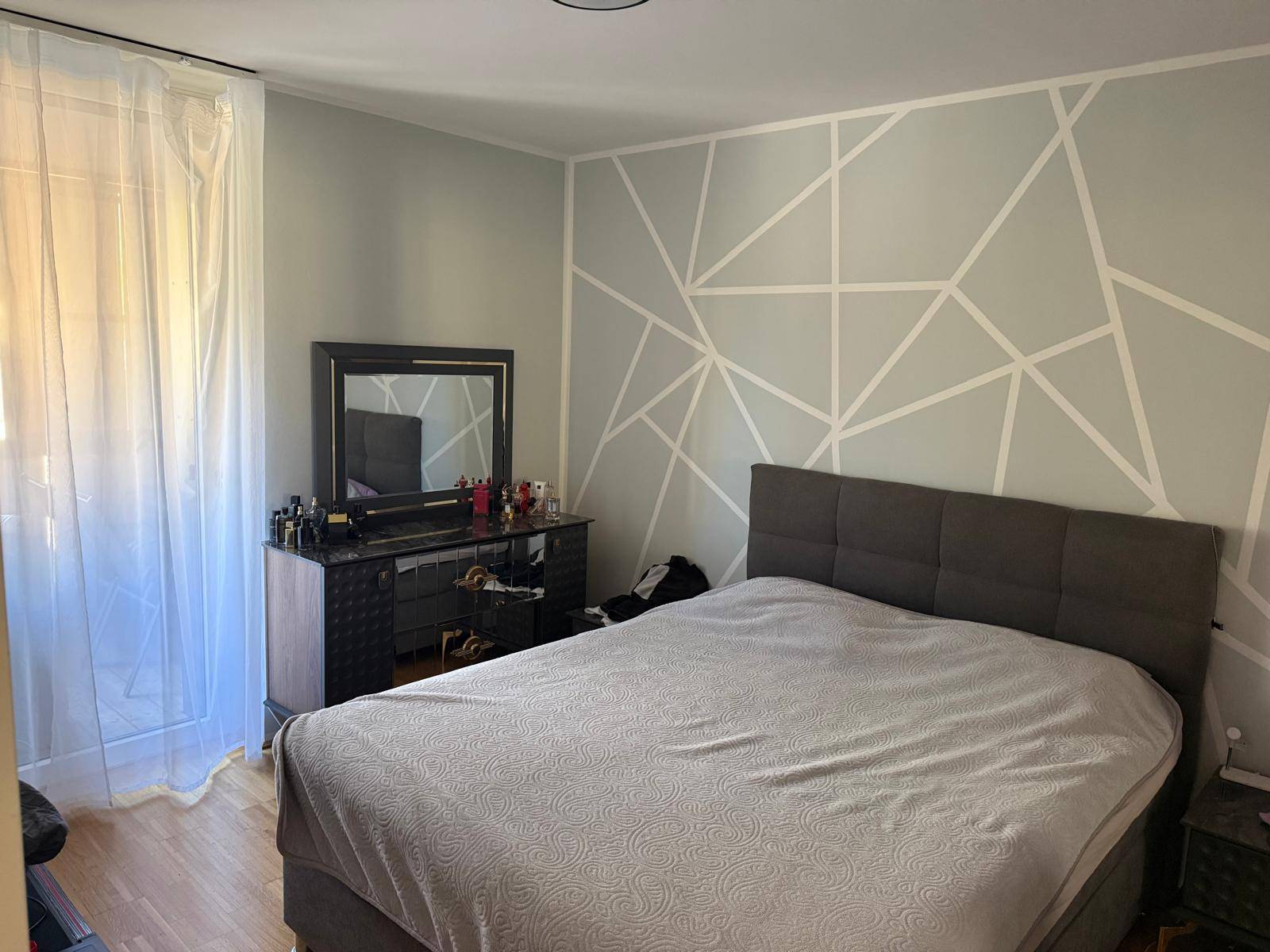 Schlafzimmer mit modernem geometrischem Wandmuster, großem Bett und Holzparkettboden.