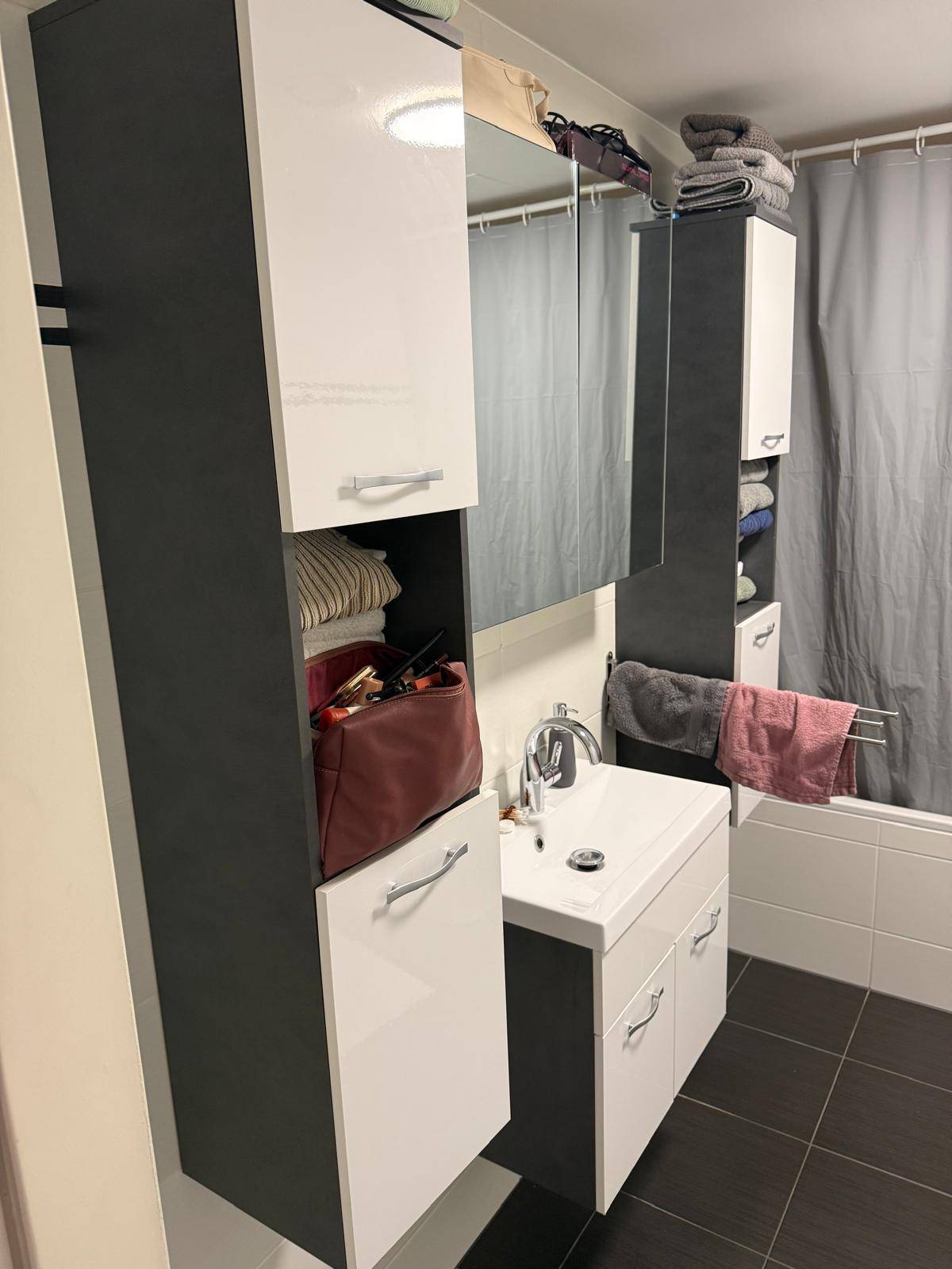 Modernes Badezimmer mit Waschtisch, Spiegelschrank, viel Stauraum und einer Badewanne mit Duschvorhang.