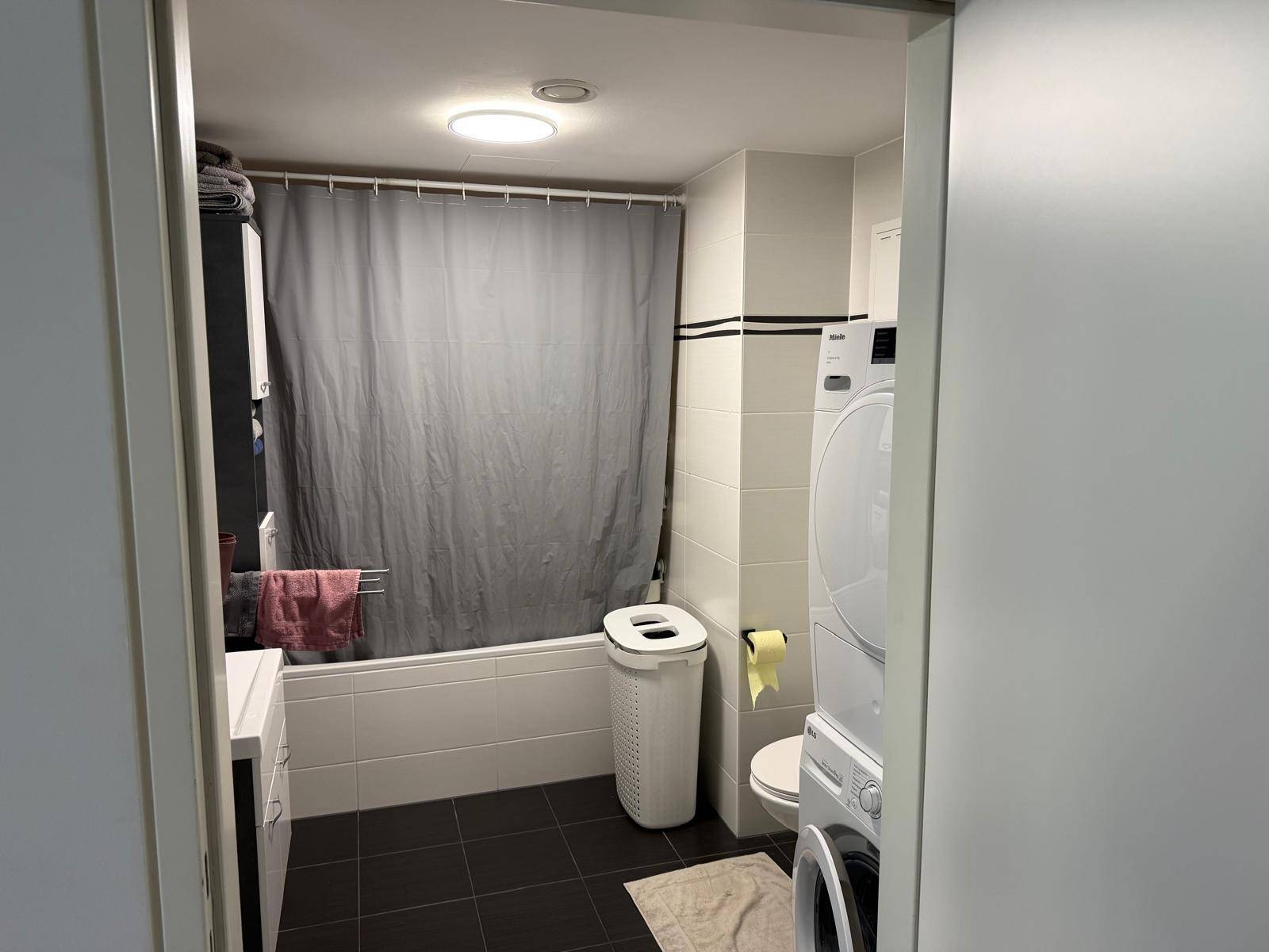 Funktionales Badezimmer mit Badewanne, Toilette und integrierter Waschmaschine sowie Trockner.