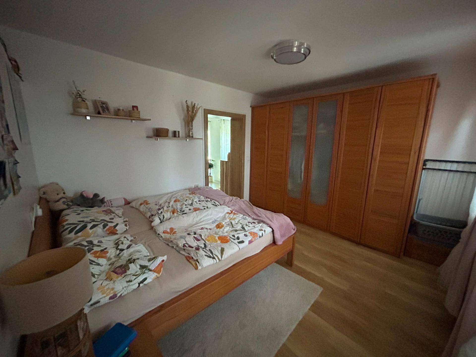 Schlafzimmer mit hellem Holzbett, floraler Bettwäsche und großem Holzschrank.