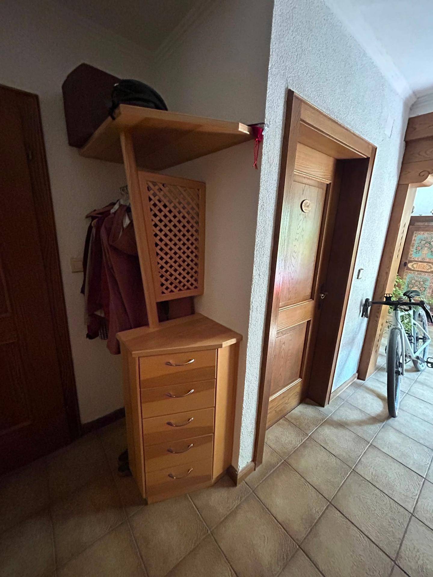 Eingangsbereich mit Holzgarderobe, Kommode und Fliesenboden, der zu weiteren Räumen führt.