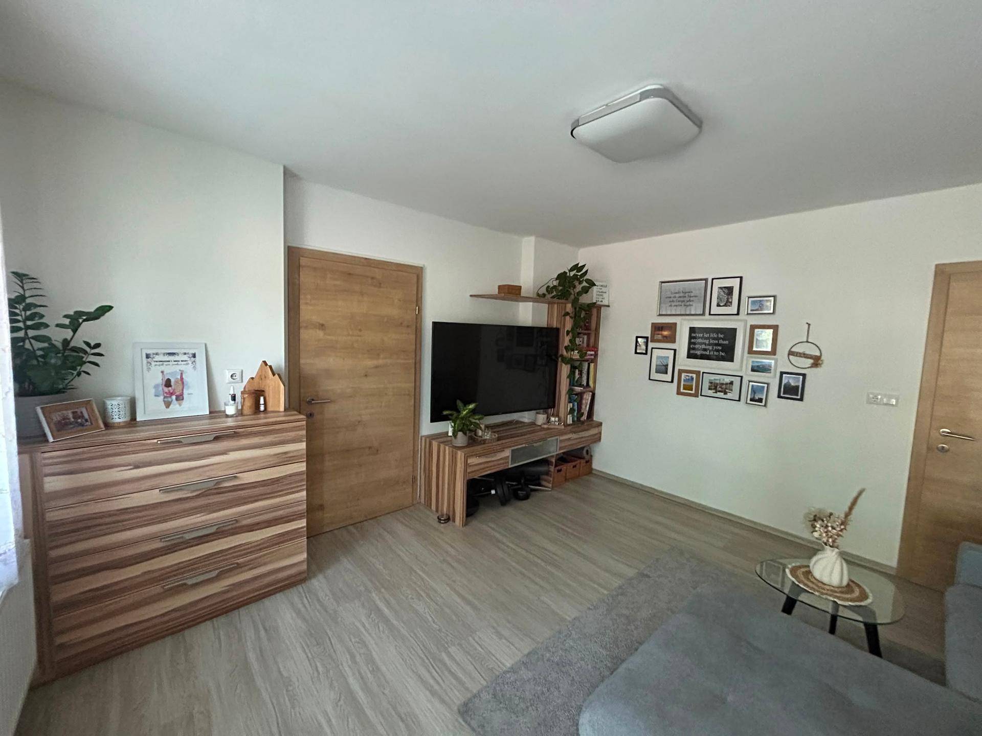 Helles Wohnzimmer mit modernem TV-Möbel, Holzakzenten und dekorativen Bilderrahmen an der Wand.