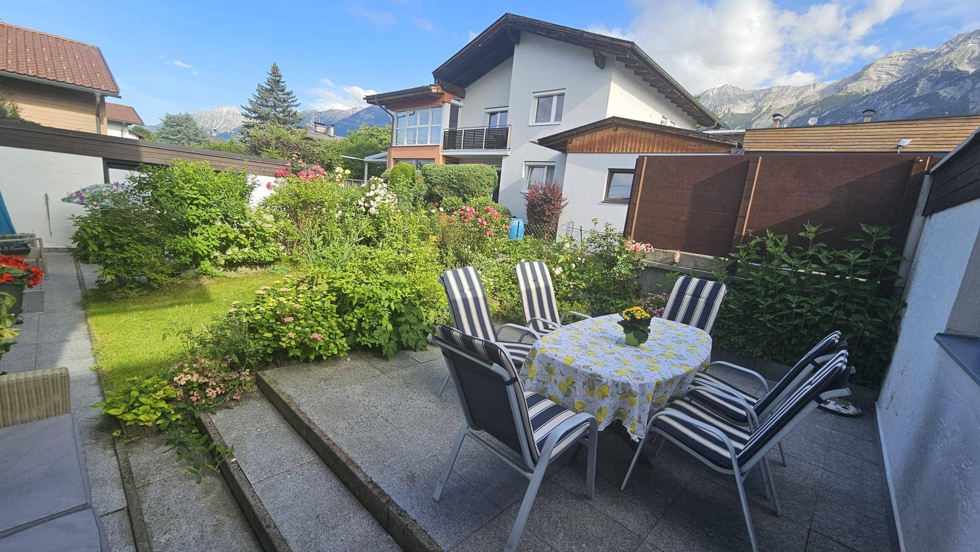 Gepflegter Garten mit Rasenfläche, Blumenbeeten und einer gemütlichen Sitzecke im Freien mit Bergblick.