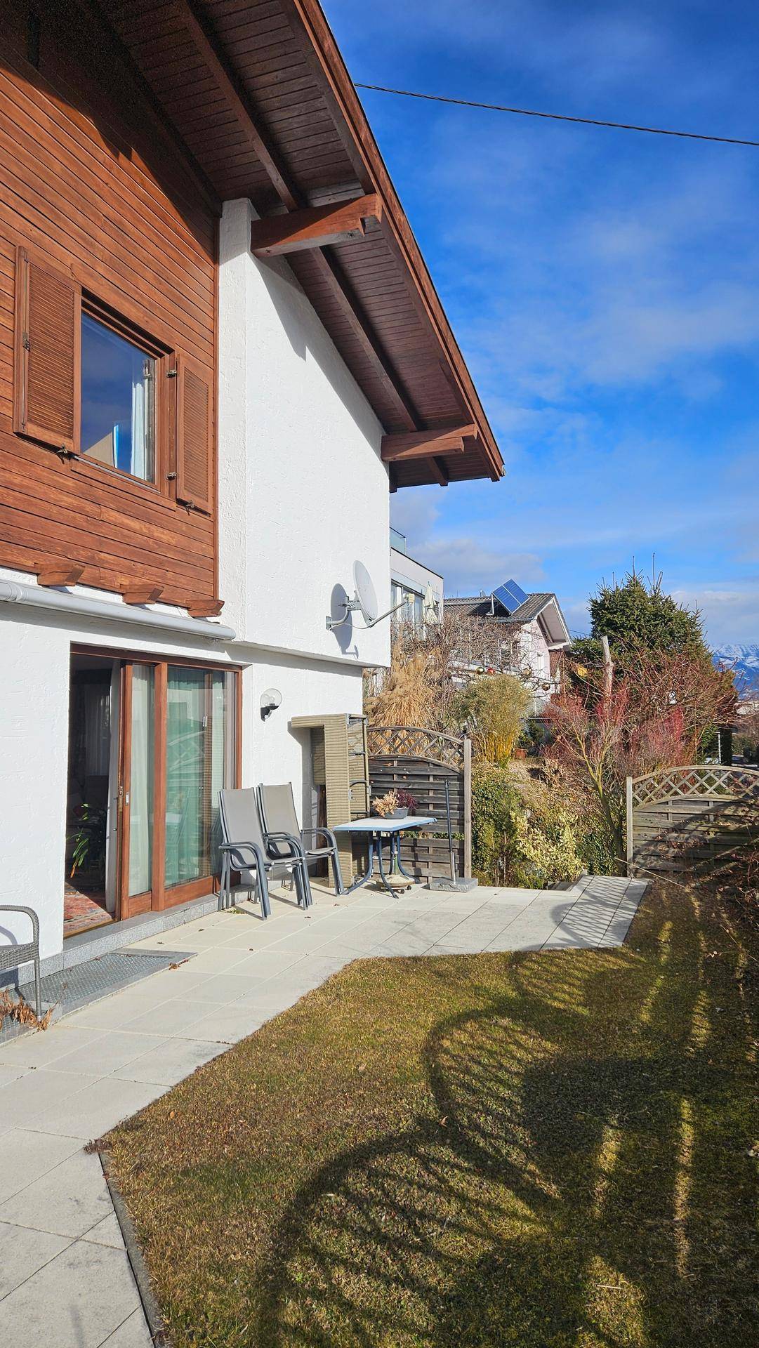 Sonniger Terrassenbereich mit Sitzgelegenheiten, Zugang zum Garten und weitem Bergblick.
