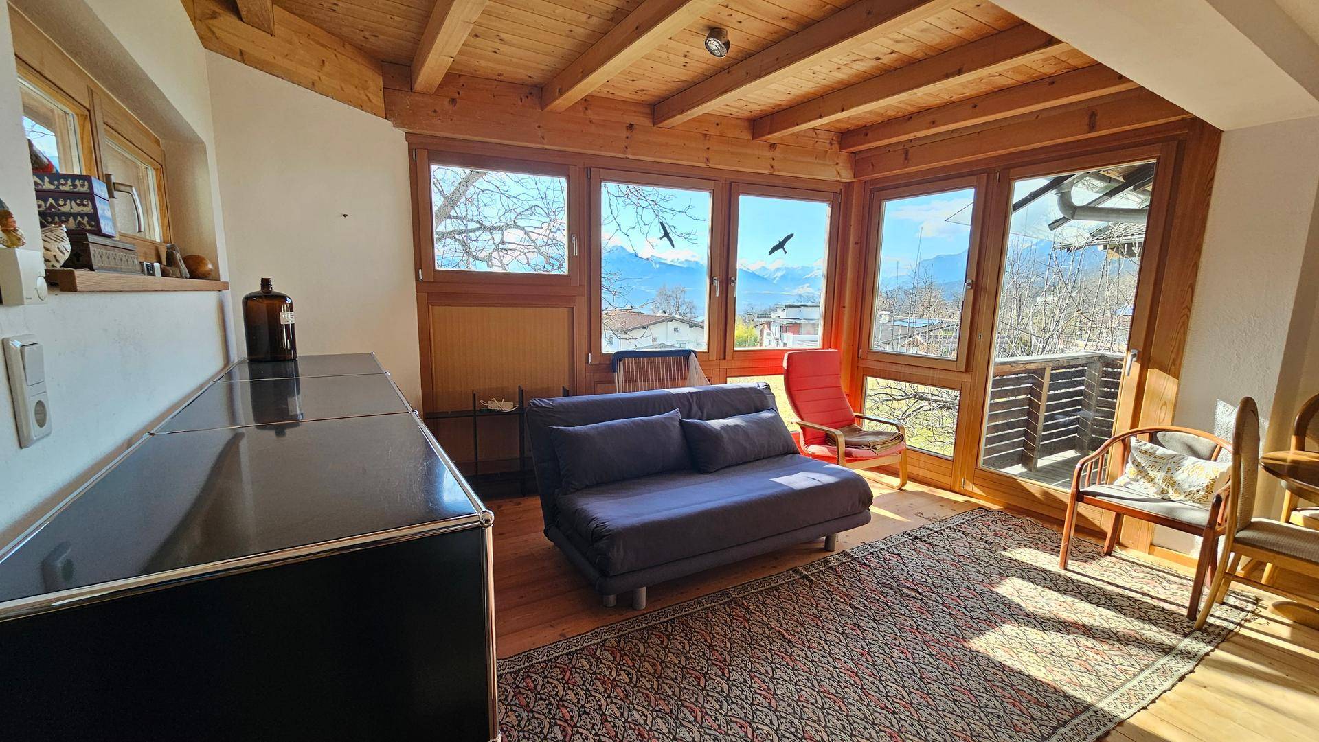 Helles Wohnzimmer mit Holzbalkendecke, großen Fenstern und weitem Blick auf die Berge.