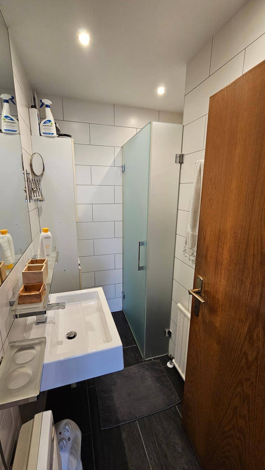 Modernes Badezimmer mit weiß gefliesten Wänden, Einzelwaschbecken und einer Duschkabine.