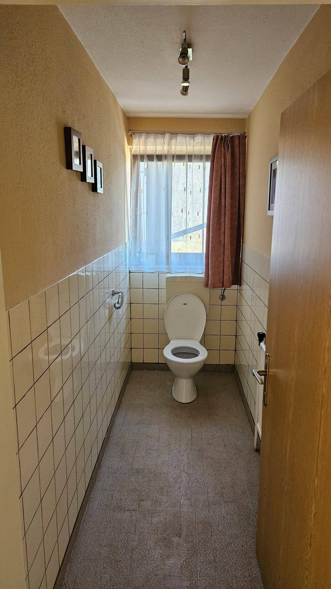 Kleines Gäste-WC mit Fenster, weißen Wandfliesen und beigefarbener Tapete.
