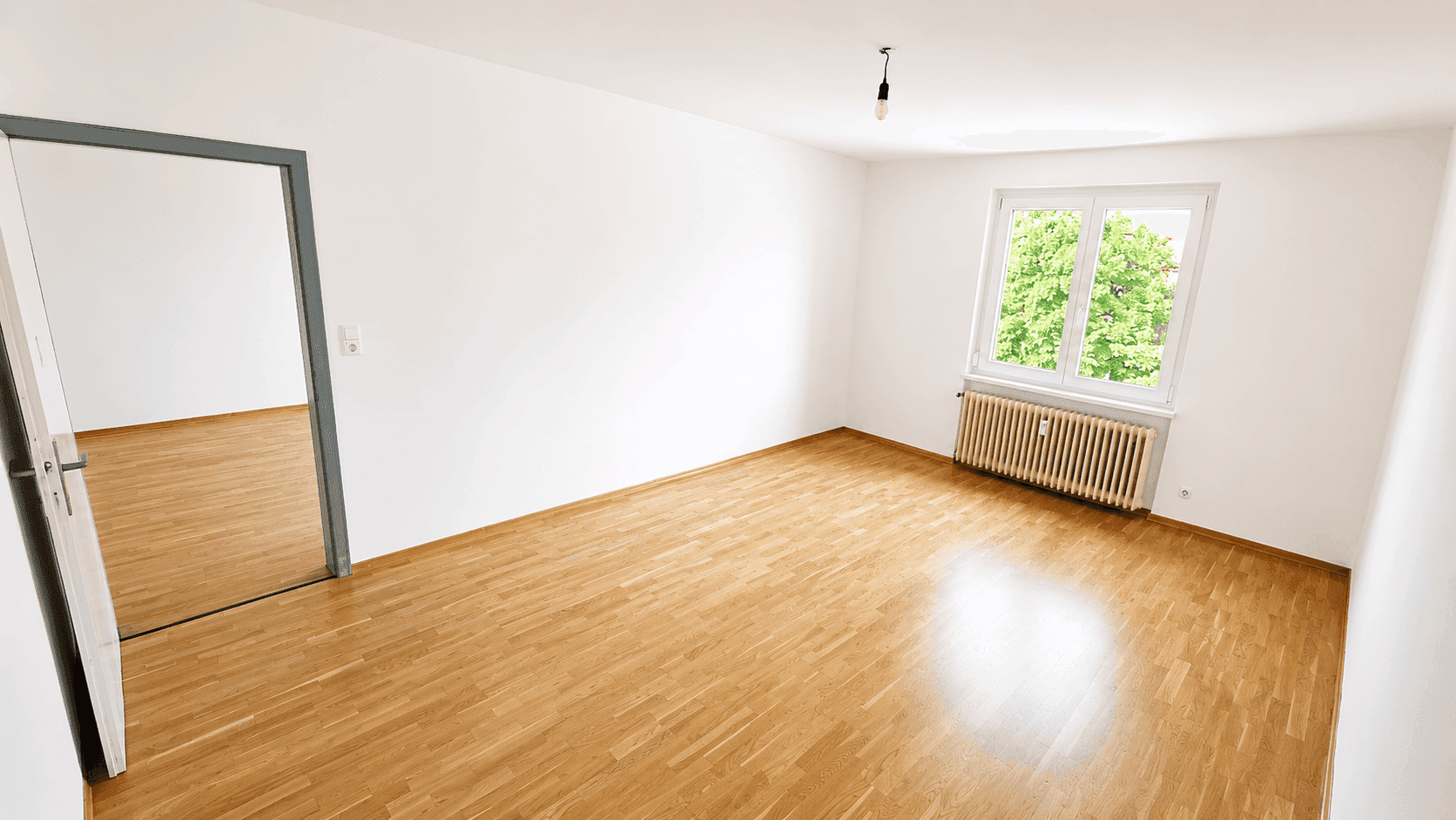 Geräumiges Zimmer mit Holzparkett, einem großen Fenster und Blick ins Grüne.