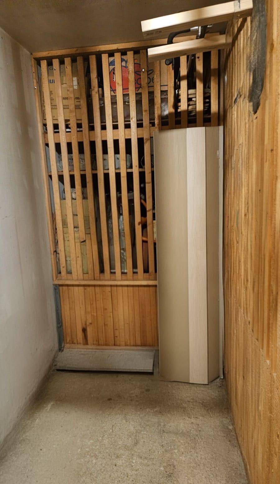 Praktischer Abstellraum oder Kellerabteil mit Holzlattenwänden und Betonboden für zusätzlichen Stauraum.