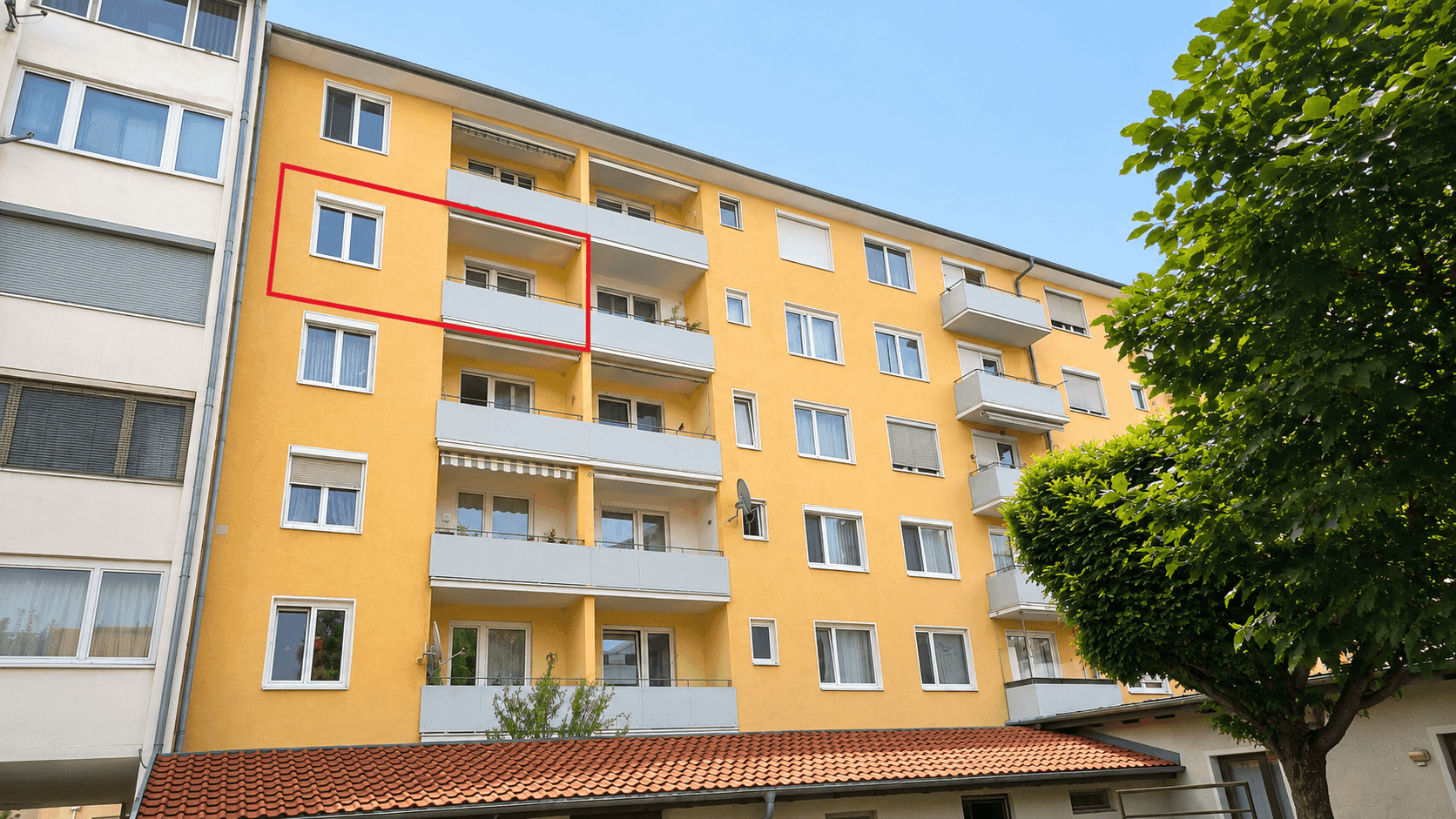 Gelbes Mehrfamilienhaus mit Balkonen und großen Fenstern in einer städtischen Umgebung.