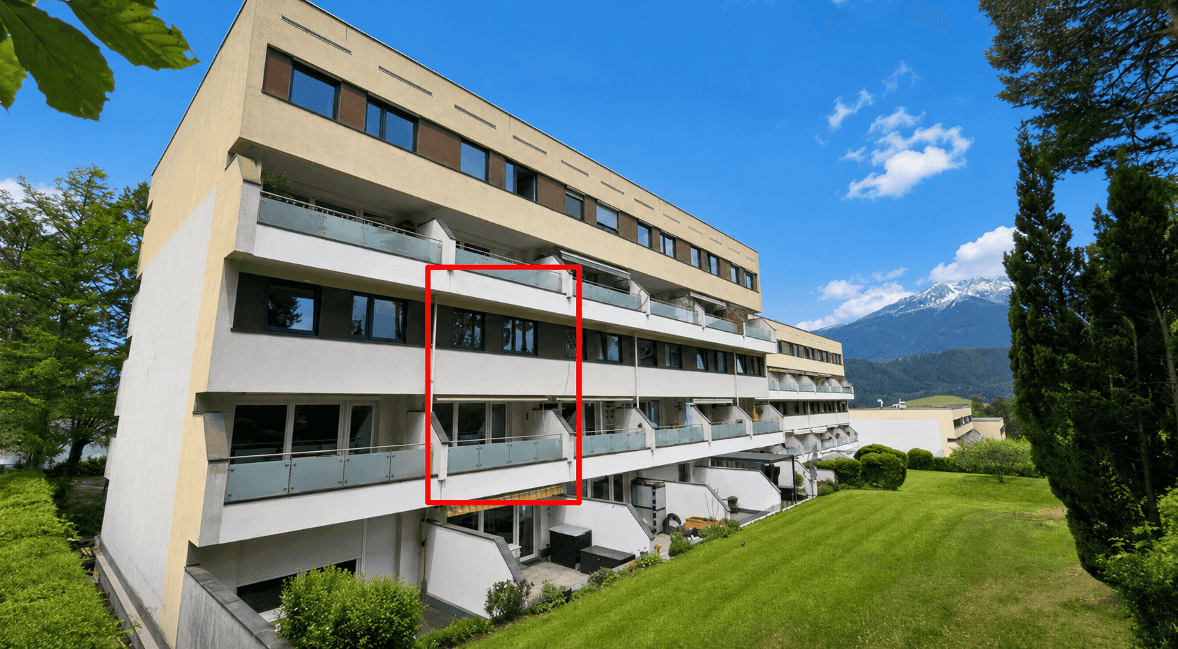 Moderne Wohnanlage mit Balkonen, umgeben von Grünflächen und mit beeindruckendem Bergblick.