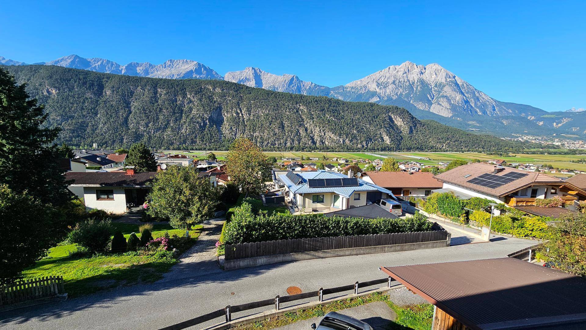 Panoramablick über eine Siedlung mit Häusern und majestätischen Bergen im Hintergrund unter blauem Himmel.