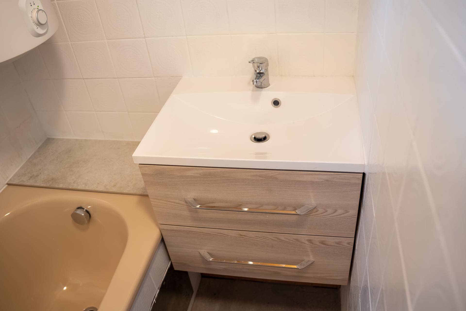 Waschtisch mit Einzelwaschbecken und Holzunterschrank neben einer beigefarbenen Badewanne.