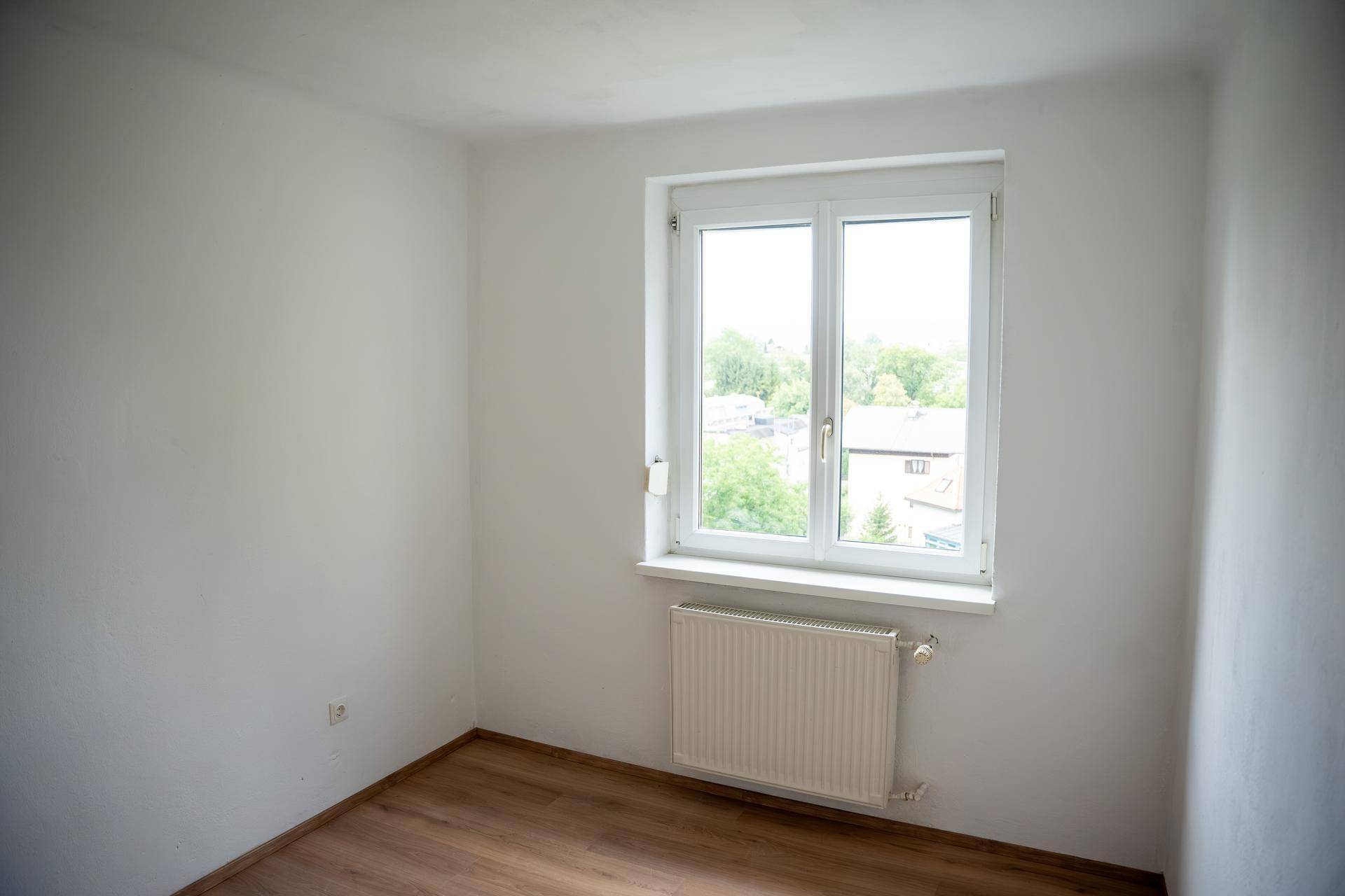 Helles Zimmer mit Laminatboden, Fenster und Heizkörper, bietet einen Blick ins Grüne.