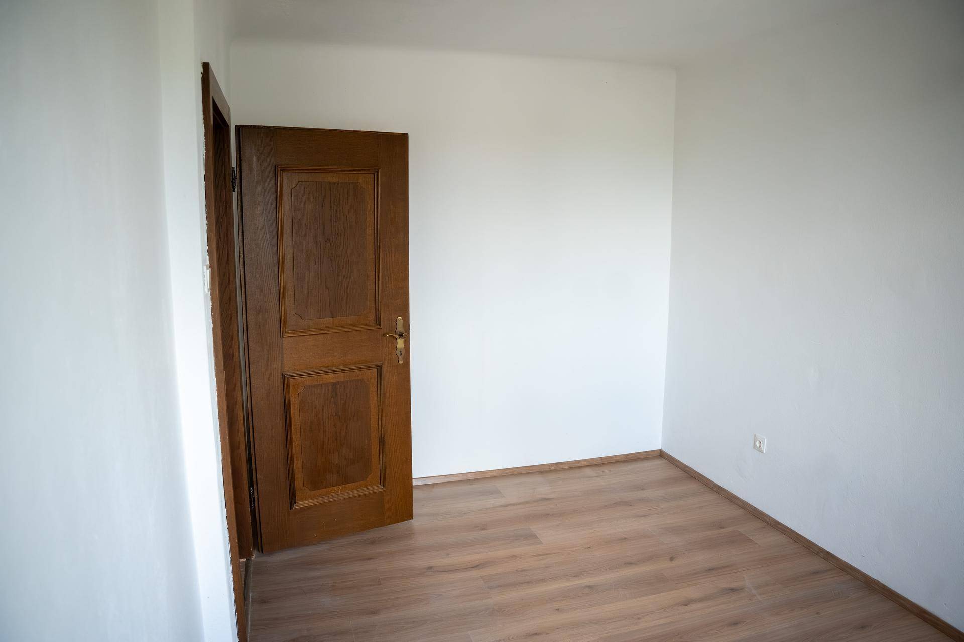 Leeres Zimmer mit Laminatboden und einer klassischen Holztür, bereit zur individuellen Gestaltung.