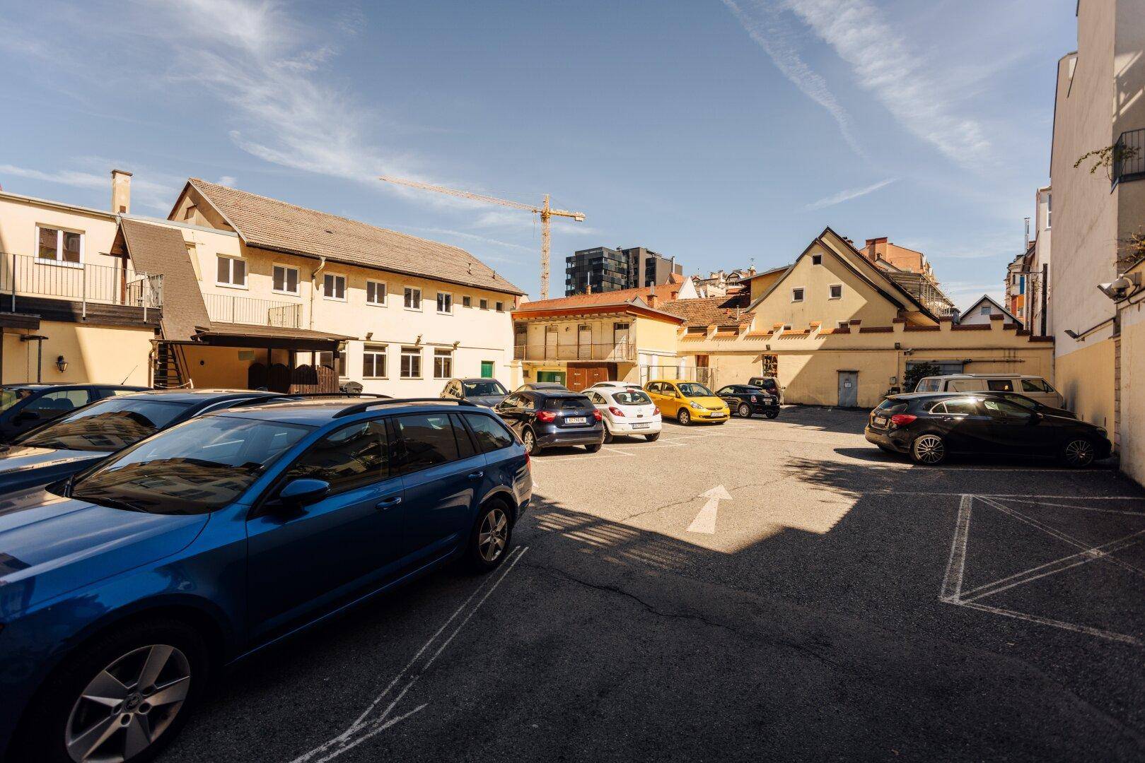 Außenparkplatz mit mehreren Autos, umgeben von Gebäuden, unter einem klaren blauen Himmel.