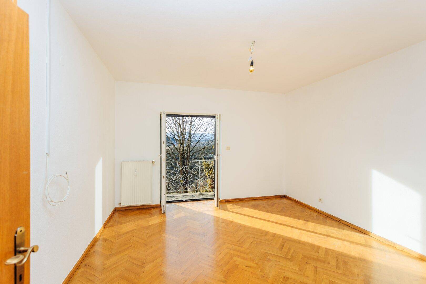 Helles Zimmer mit Fischgrätparkett und Zugang zu einem Balkon mit weitem Ausblick.