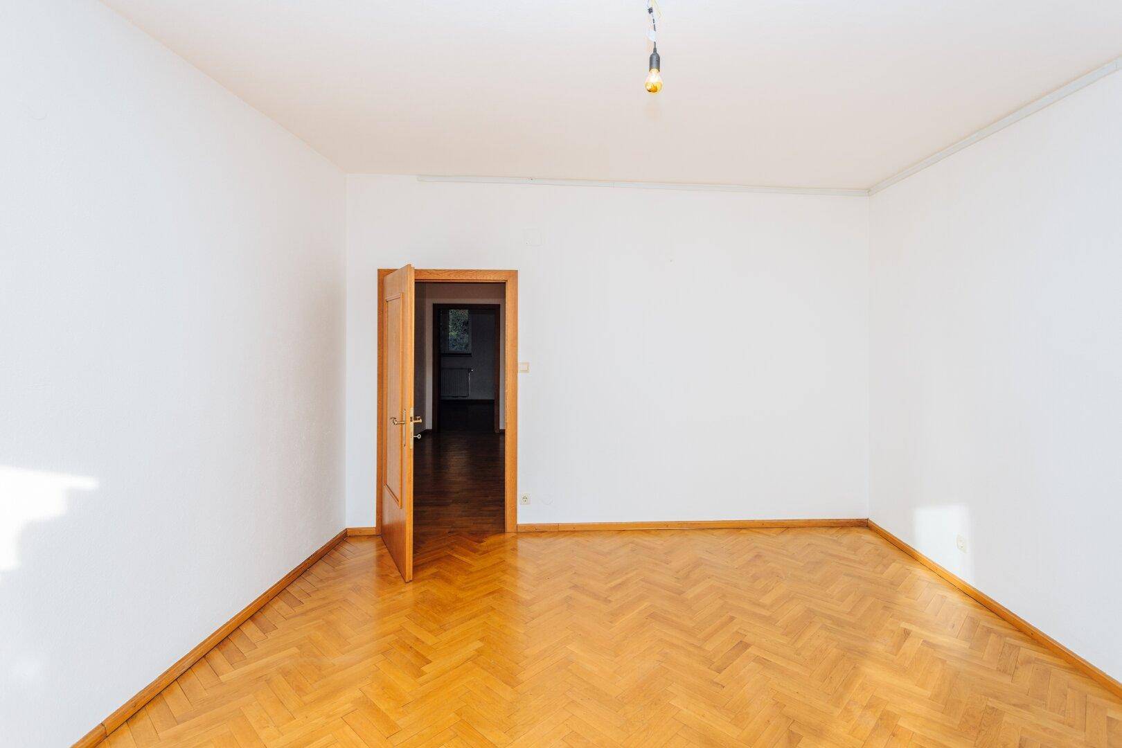 Leeres Zimmer mit Fischgrätparkett und Holztür, bereit für individuelle Gestaltung.