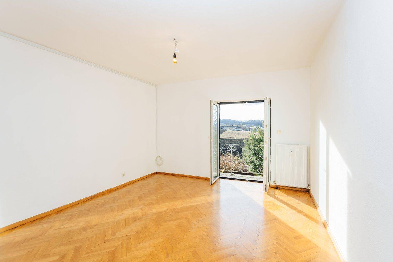 Lichtdurchflutetes Zimmer mit Fischgrätparkett und Zugang zu einem Balkon mit Aussicht.