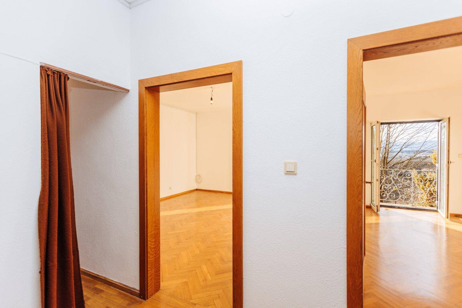 Flur mit Parkettboden und Holztüren, der einen Blick in angrenzende helle Zimmer bietet.