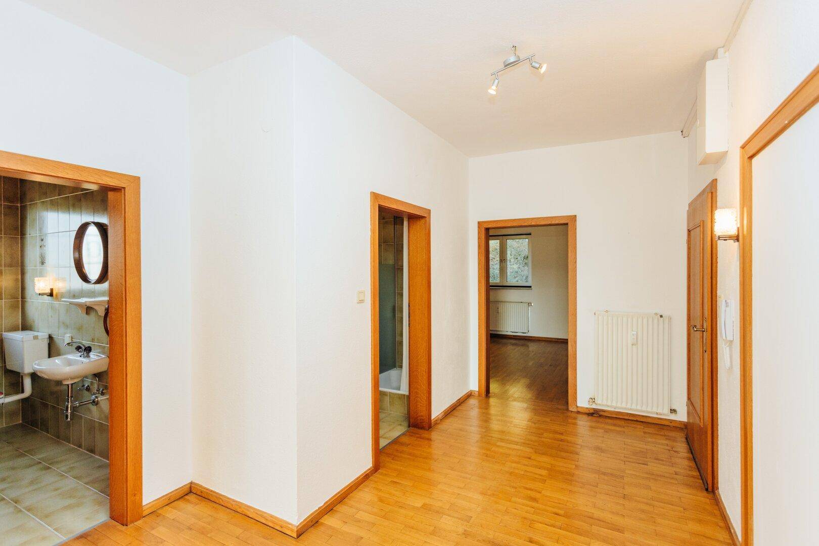 Flur mit Parkettboden und Zugang zu einem gefliesten Badezimmer mit Fenster.